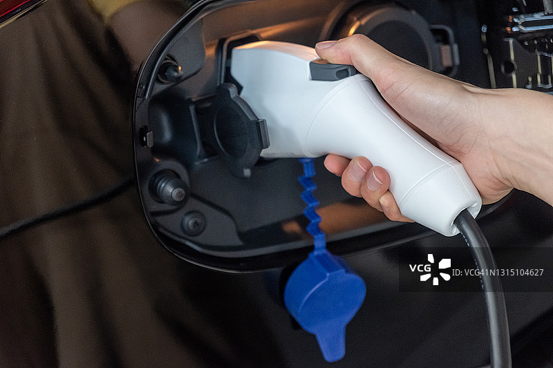 手持电缆将插电式混合动力汽车连接到充电端口的特写图片素材