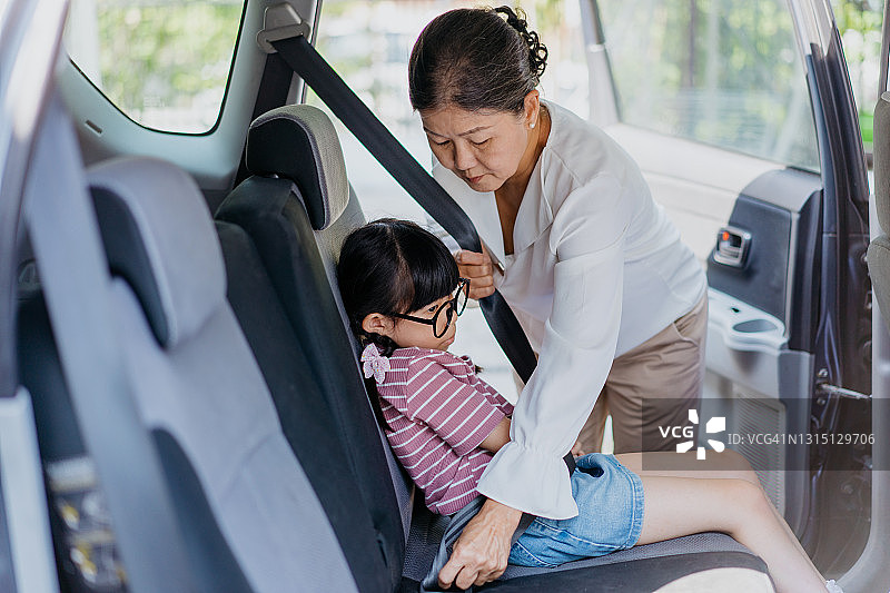 年长的亚裔妇女在车里为孙女系好安全带图片素材
