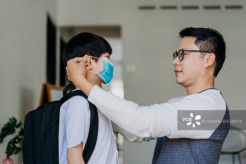 亚洲男人帮助儿子戴防护口罩图片素材