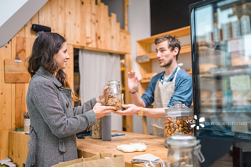 30多岁的男店员在可持续商店里用可重复使用的罐子销售商品图片素材