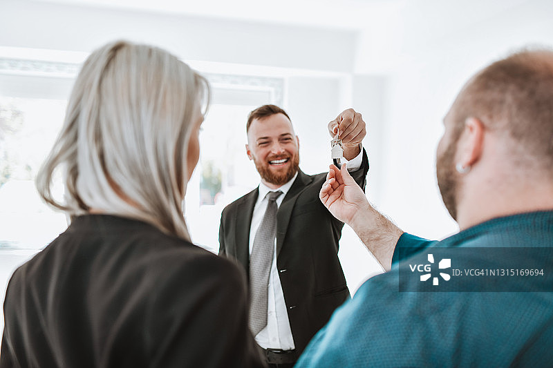 情侣从微笑的房地产经纪人手中接过钥匙图片素材