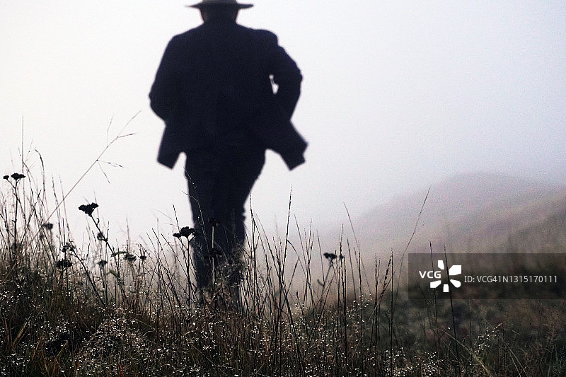 戴着经典软呢帽和长外套的男人在雾天乡村奔跑图片素材