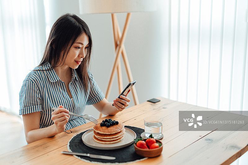 在家吃早餐时使用智能手机的年轻女人图片素材