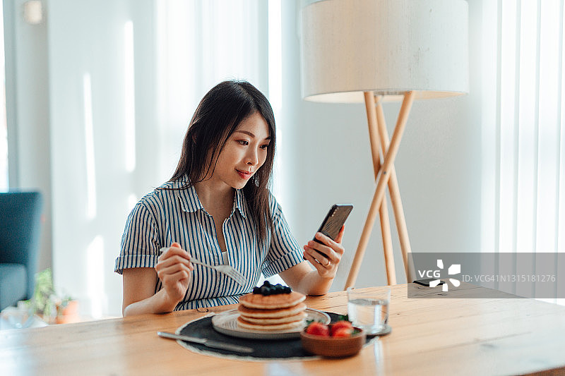 在家吃早餐时使用智能手机的年轻女人图片素材