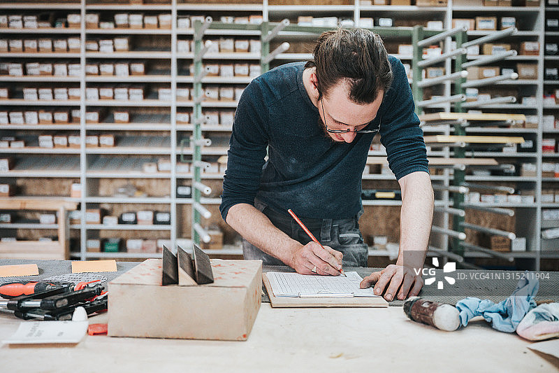 年轻木匠在车间的工作台上写笔记图片素材