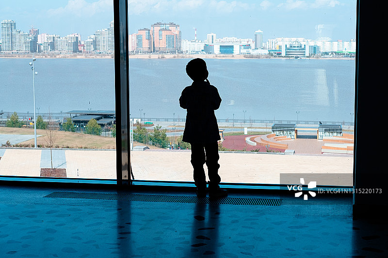 机场男孩的剪影，透过宽大的窗户俯瞰城市和海景图片素材