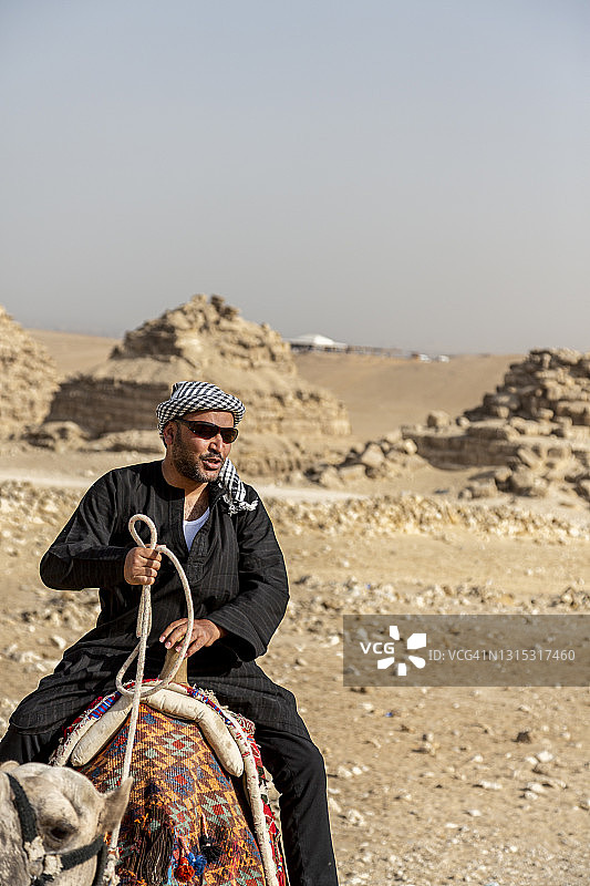 英俊男人骑着骆驼在沙漠中——吉萨金字塔图片素材