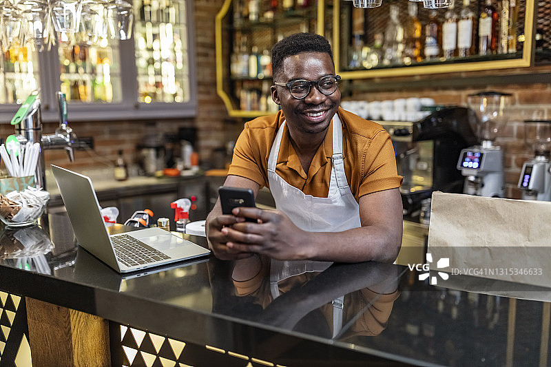 英俊的酒吧男服务员在咖啡馆里使用手机图片素材