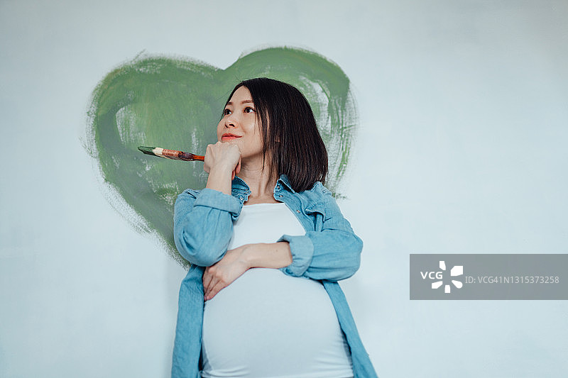 怀孕的女人用油漆刷装修婴儿房图片素材