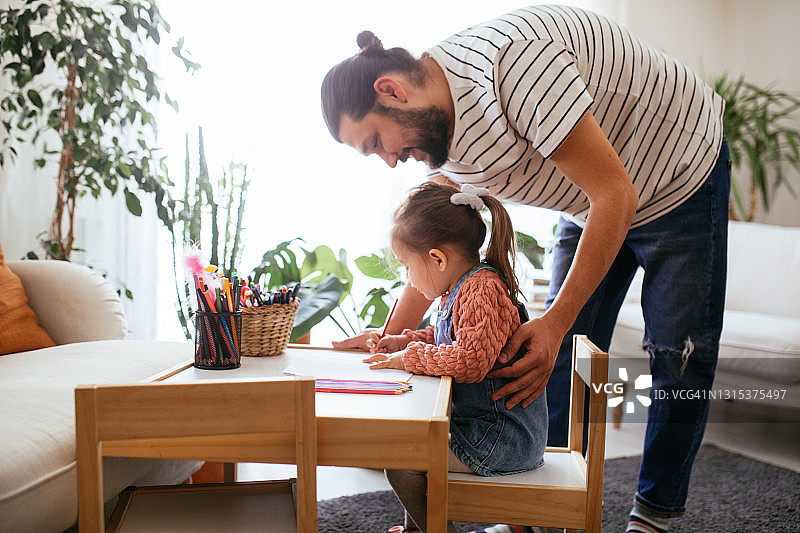 快乐的父亲辅导女儿做功课，小女孩在家做作业图片素材