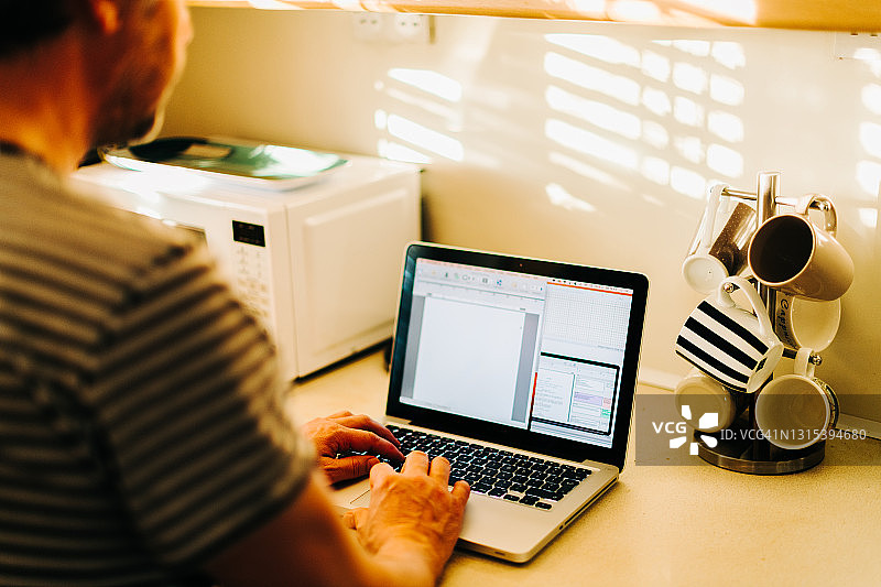 一名男子在郊区厨房的笔记本电脑上工作图片素材