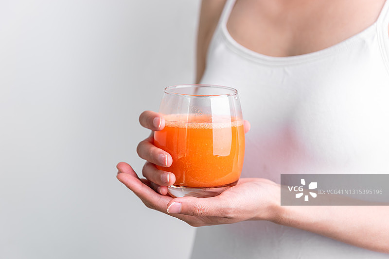 饮用新鲜胡萝卜蔬菜汁的女人，手持新鲜胡萝卜汁图片素材