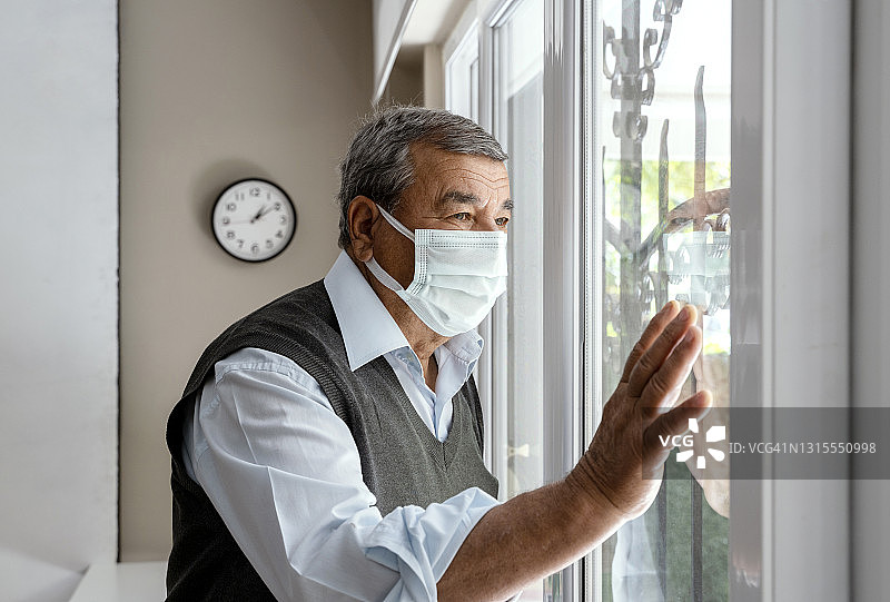 在冠状病毒爆发期间，戴着防护口罩的年长男人在家隔离图片素材