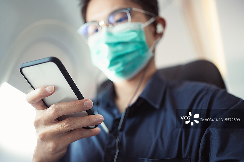 亚洲商务人士在飞机上旅行时戴着口罩使用手机进行股票交易图片素材