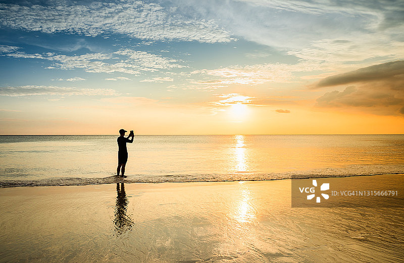 日落时分在海滩上使用平板电脑的年轻男人图片素材