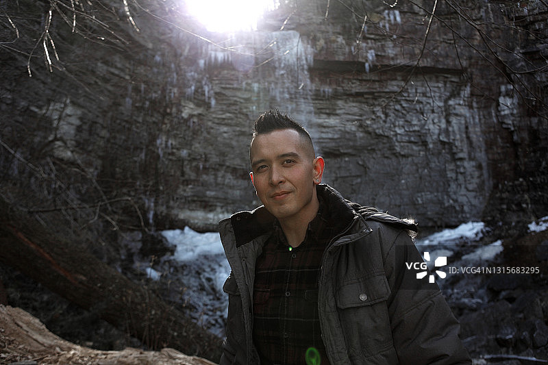 男子在冰冻瀑布附近的树林里徒步的肖像图片素材