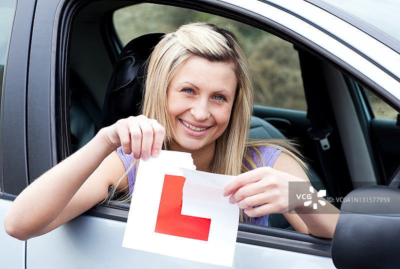 快乐的年轻女司机撕掉她的L标志图片素材