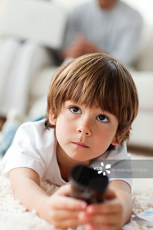 专注的小男孩躺在地板上看电视图片素材