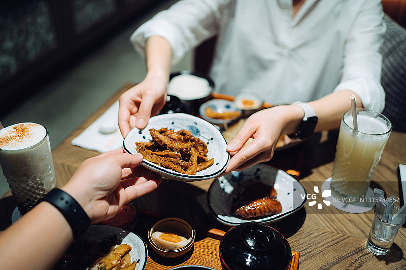 年轻女子在餐厅用餐时将食物传递给男友，一同品尝美味的中国台湾美食图片素材