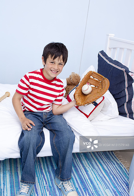 在卧室里玩棒球的微笑小男孩图片素材