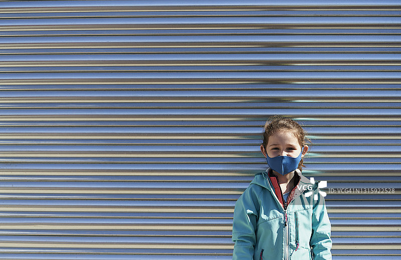 戴口罩站在金属墙前的微笑少女图片素材