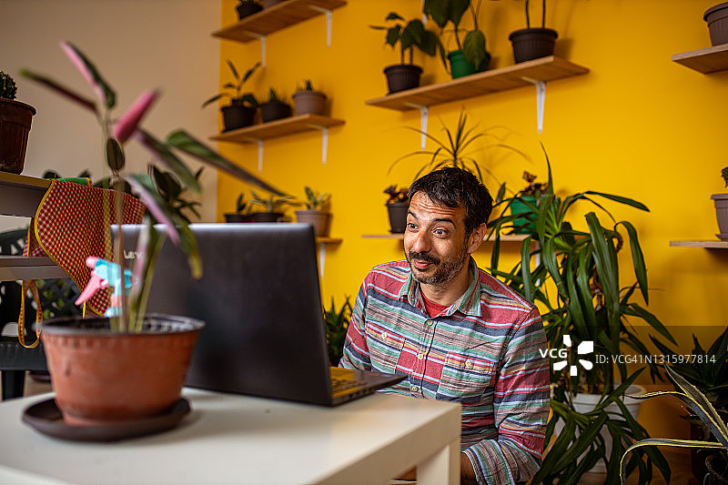 在室内花园里用笔记本电脑工作的年轻男人图片素材
