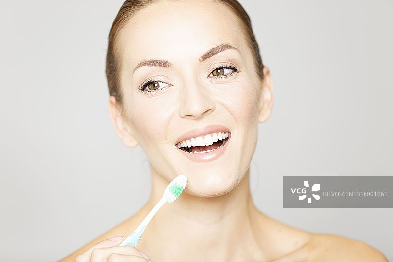 以美容姿势拿着牙刷微笑的年轻女人图片素材