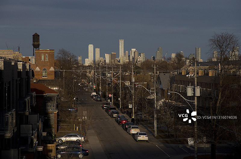 停在安静住宅街道上的汽车，远处是城市天际线图片素材