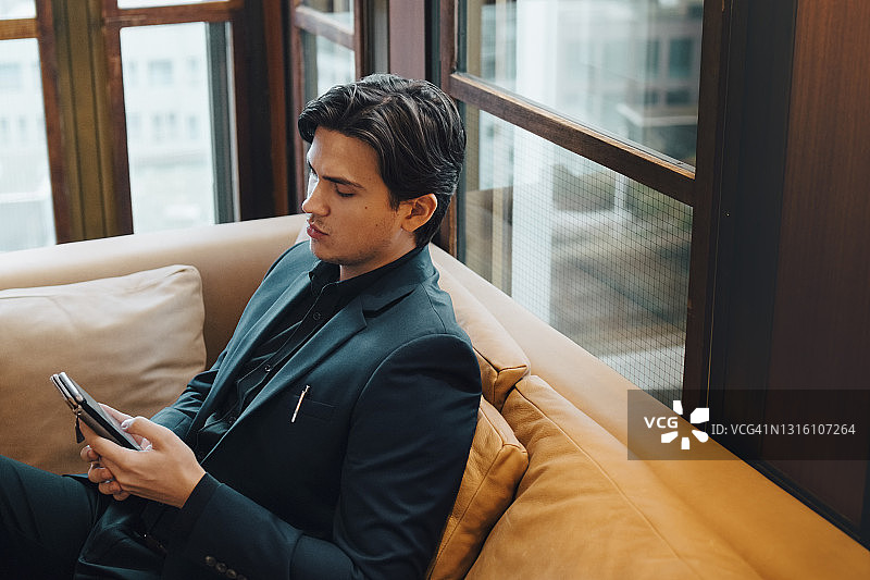 在办公室沙发上使用智能手机的男人图片素材
