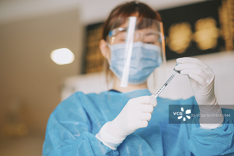 戴着PPE防护服和外科手套的亚裔女医生准备接种新冠疫苗图片素材