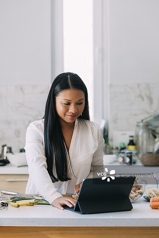 亚洲年轻美食博主一边研究食谱，一边在平板电脑上看她最喜欢的烹饪节目图片素材
