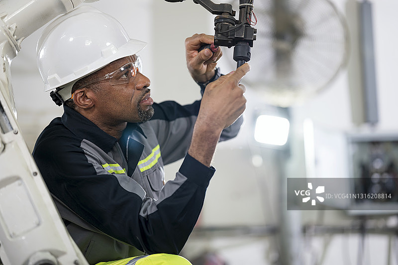 年长的非洲工程师在工程零件生产线上安装机器人弧焊枪，提高生产力和质量控制图片素材