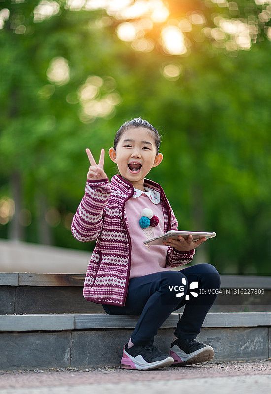 小女孩拿着平板电脑，做出和平手势图片素材
