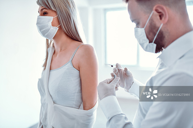 年轻女人接种新冠疫苗，男医生操作图片素材