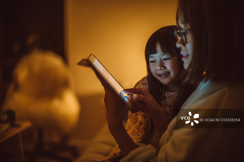 母女俩晚上在家里的沙发上一起快乐地使用平板电脑图片素材