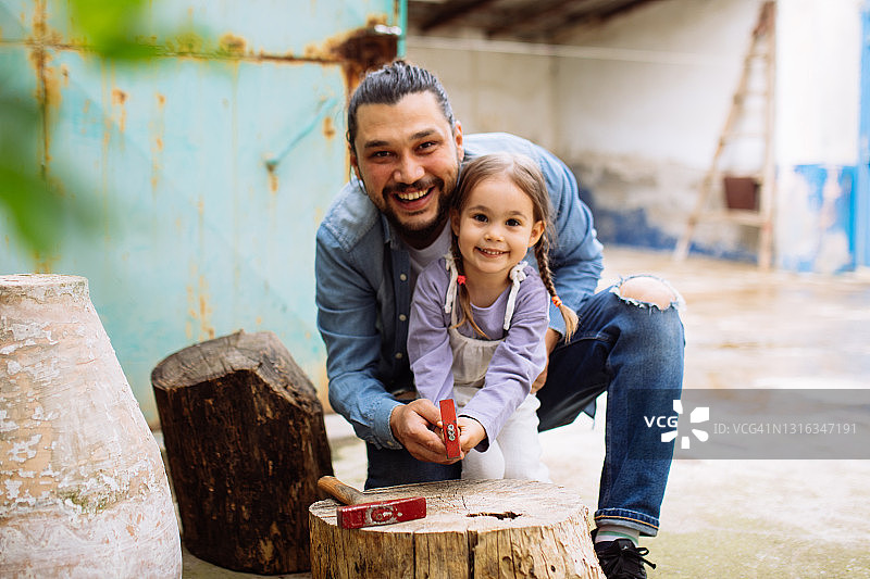 年轻的父亲在后院教女儿使用锤子图片素材