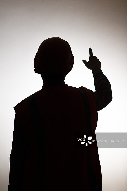 年轻建筑工人在安全帽中的背影剪影（指示方向，目标概念，工头控制工作）图片素材