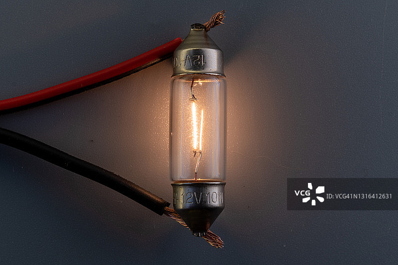经典汽车卤素灯泡，灯丝、玻璃和金属，高能耗，灰色背景，室内照明，通电工作状态，灯火通明图片素材
