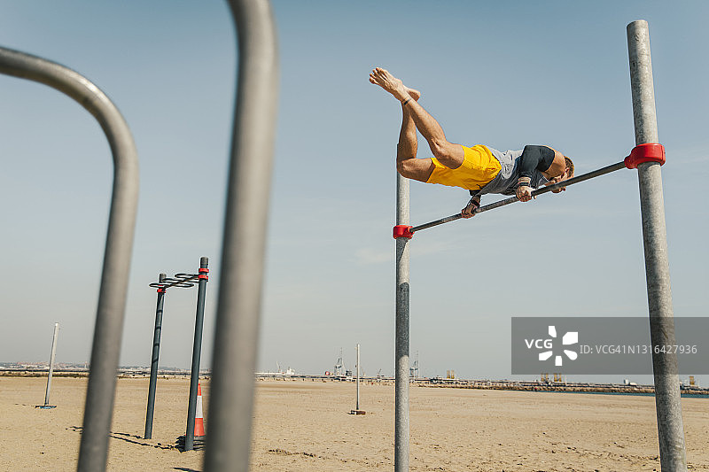 在海滩高杠上保持平衡的男运动员图片素材