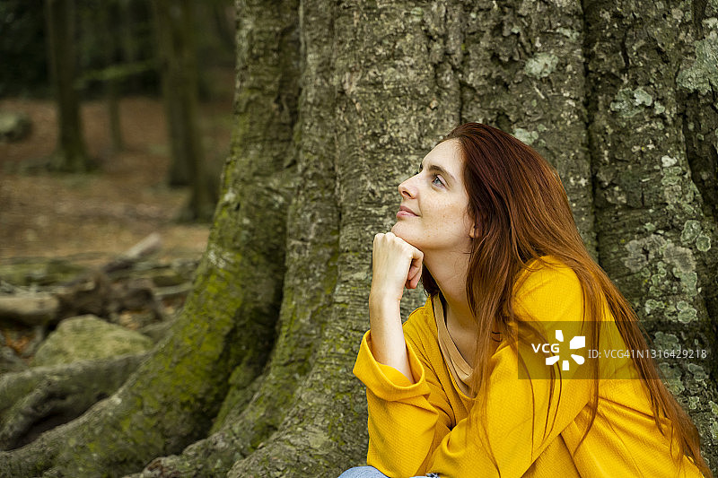 年轻女人在森林里的大树干旁做白日梦图片素材