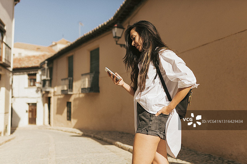 年轻女人在阳光明媚的日子里背着背包站着使用手机图片素材