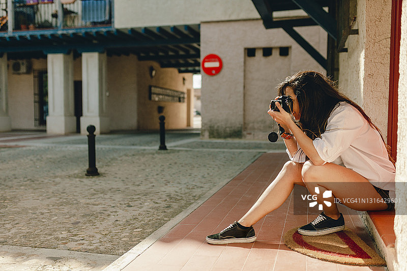 坐在人行道上用相机拍照的女人图片素材
