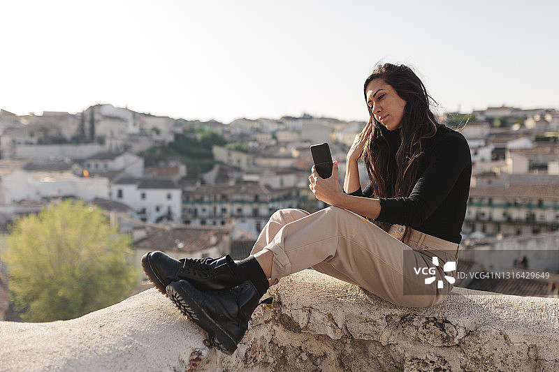坐在 retaining wall 上用手机自拍的女游客图片素材