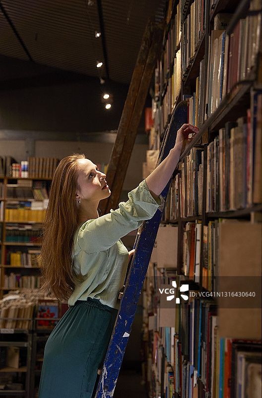 在图书馆里爬梯子找书的漂亮女人图片素材