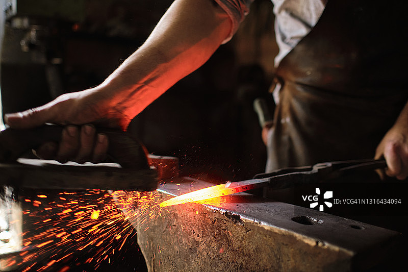 男人在铁匠铺的铁砧上锻造过热的金属图片素材