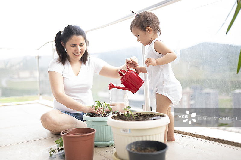 年轻母亲和她可爱的小女儿在阳台上种花图片素材