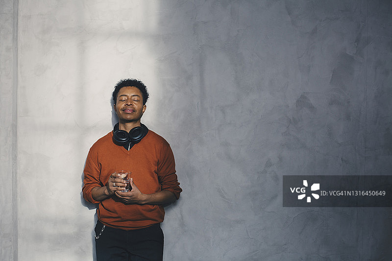 闭着眼睛靠墙站立的男商人，手持玻璃杯图片素材