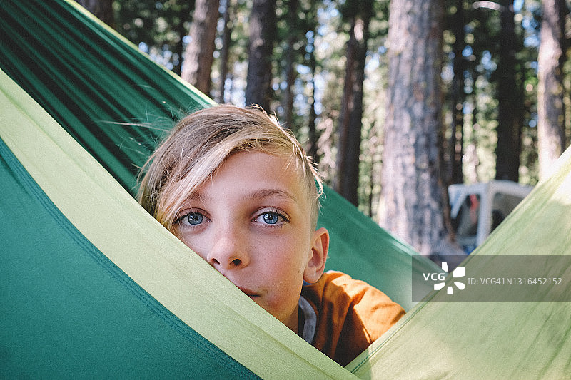 有着蓝色大眼睛的金发少女从绿色吊床后偷看图片素材