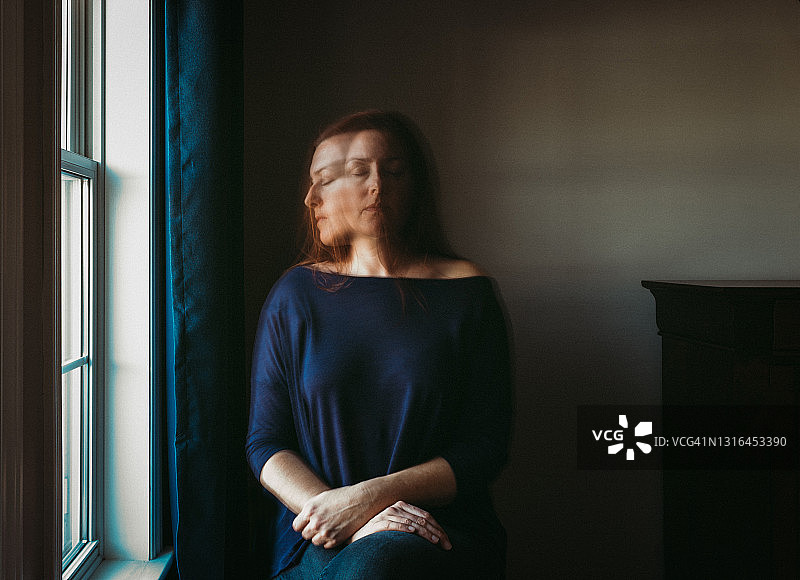 在黑暗房间窗户旁独自坐着的模糊脸女人图片素材