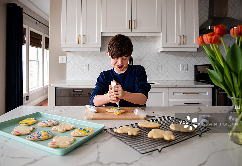 男孩在现代厨房的柜台上装饰复活节饼干图片素材